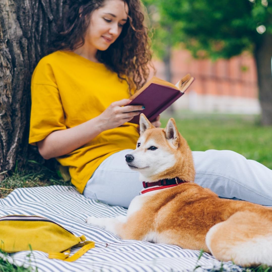 Woman sitting in a park reading a book with her dog